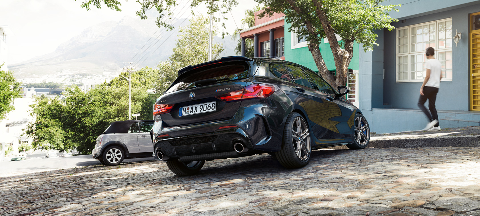 BMW M135i xDrive en Black Sapphire metallic, vista trasera de tres cuartos, estacionado frente a un edificio residencial.